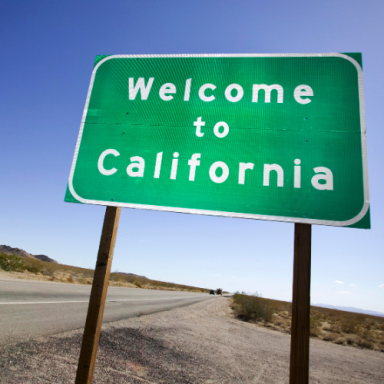 Green welcome sign for California against a clear blue sky.