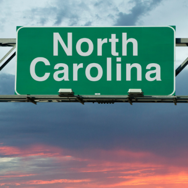 Green highway sign reading "North Carolina" against a colorful sunset sky.