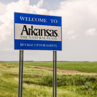 Welcome sign for Arkansas, stating "THE NATURAL STATE" with a scenic field background.