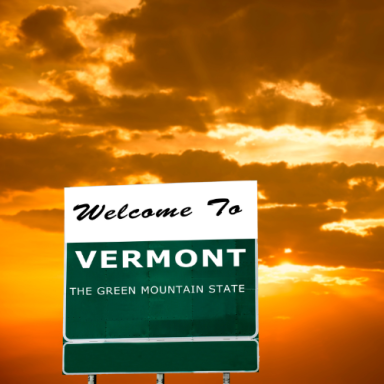 Welcome sign for Vermont against a sunset sky.