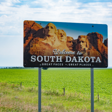 Sign welcoming visitors to South Dakota, featuring Mount Rushmore and green fields.