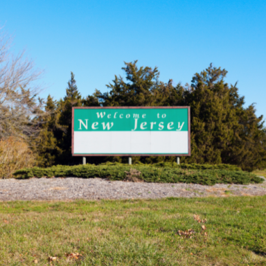 Welcome to New Jersey sign surrounded by greenery and clear blue sky.