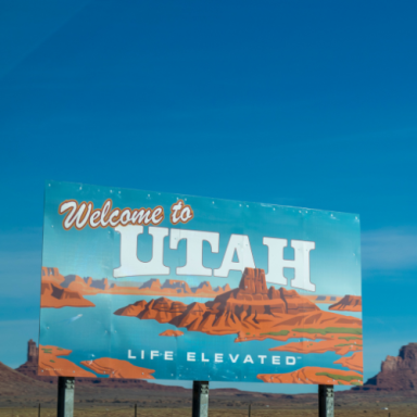 "Welcome to Utah sign with a scenic landscape and blue sky background."