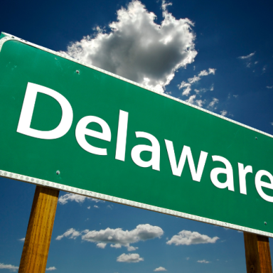 Green road sign with the word "Delaware" against a blue sky with clouds.