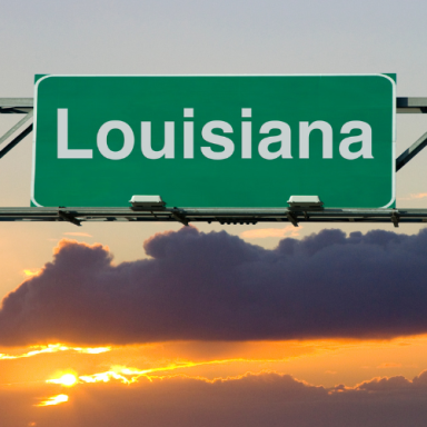 Green highway sign displaying the word "Louisiana" against a sunset backdrop.