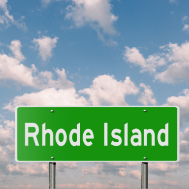 Green road sign with "Rhode Island" against a blue sky with clouds.