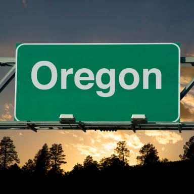 Oregon highway sign with a sunset and silhouetted trees in the background.