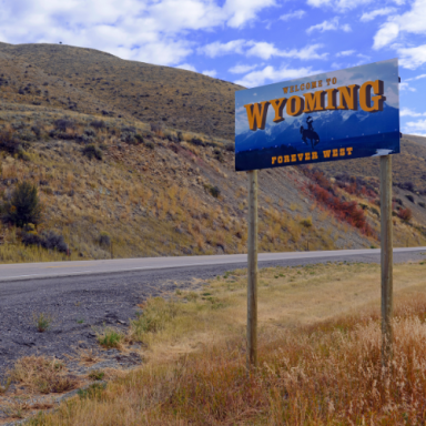 Welcome to Wyoming sign by the roadside with a scenic hilly background.