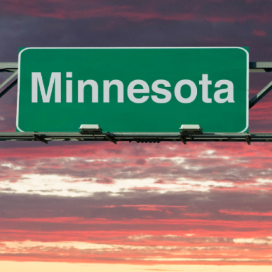 Green road sign displaying "Minnesota" against a colorful sunset sky.