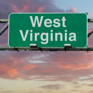 Green highway sign for West Virginia against a colorful sunset sky.