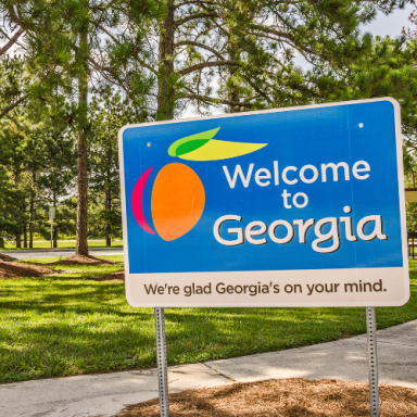 Welcome sign for Georgia featuring an orange and green design on a sunny landscape.