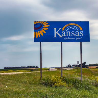 Kansas welcome sign featuring a sunflower against a cloudy sky.